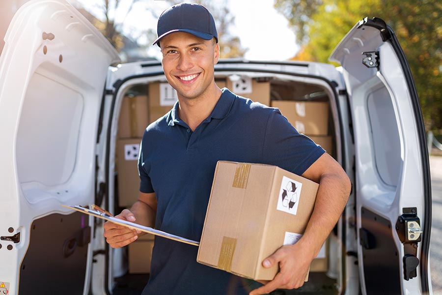 Business Insurance - Man in Blue Uniform Holds a Package and Clipboard in Front of Open Delivery Truck